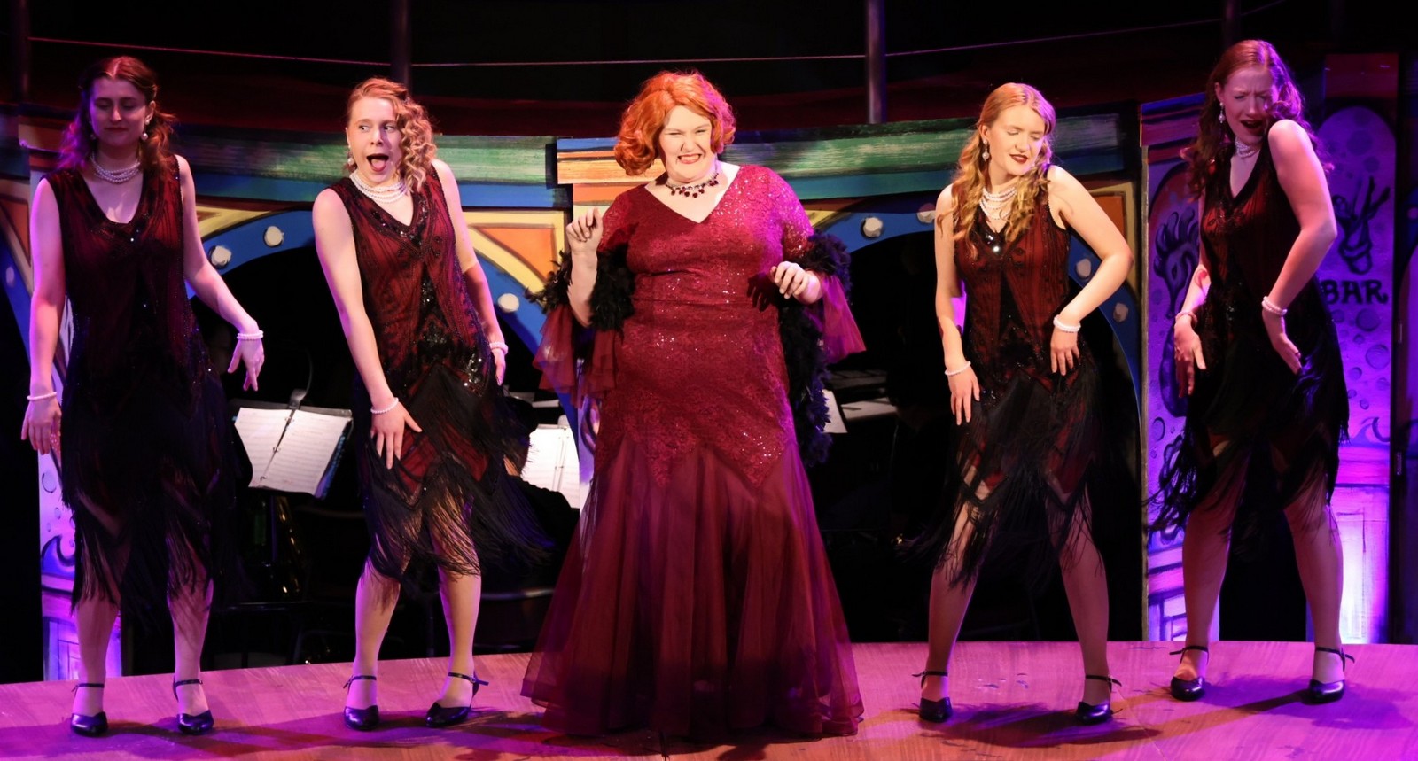 Several performers dance to a musical number in glittery gowns. 