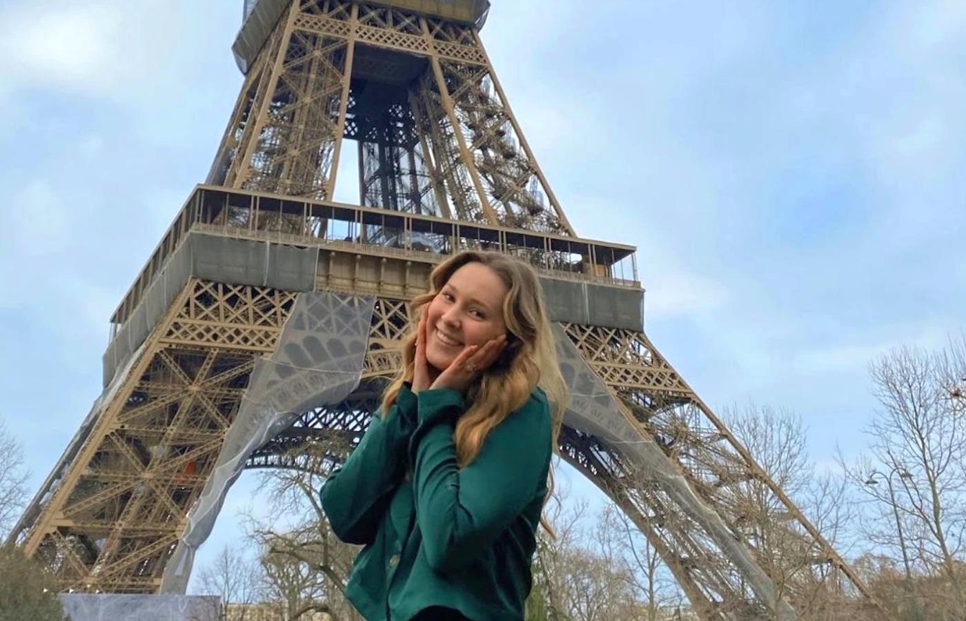A woman stands with a smile before the Eiffel Tower. 