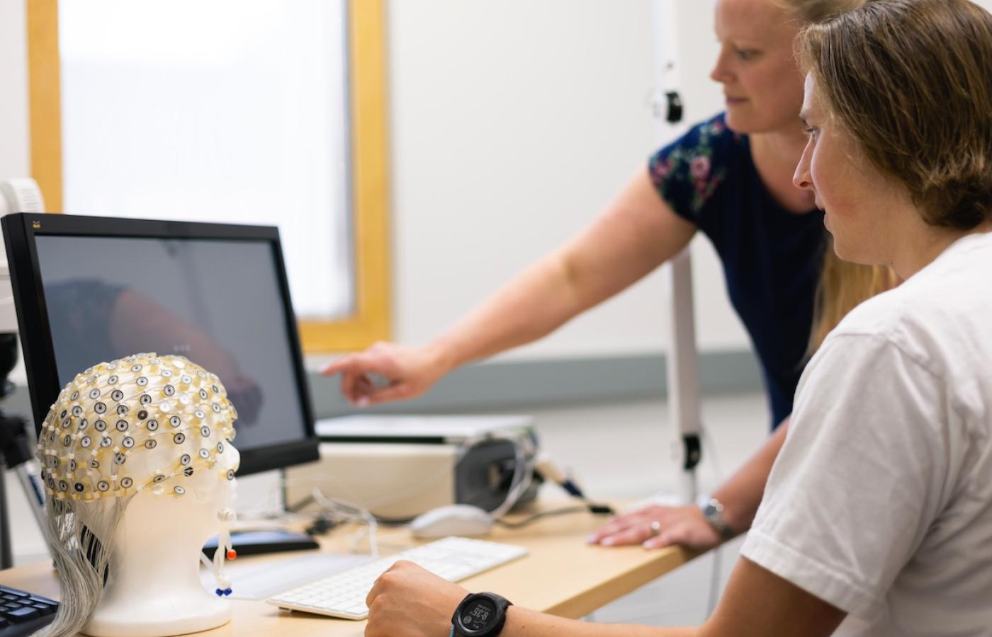 A student works with a professor and a model of a head full of electrodes. 