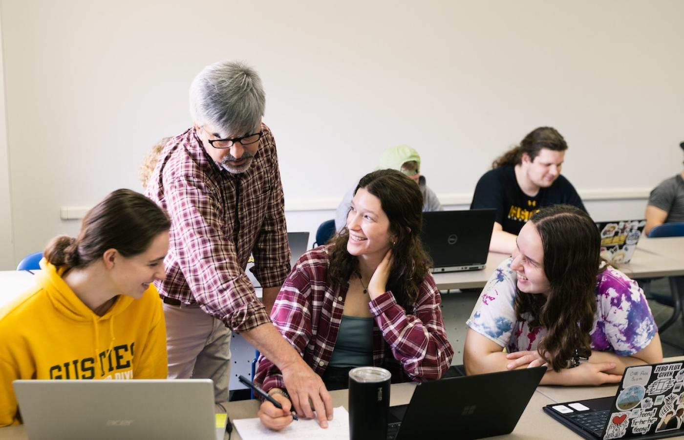 Students look at something a professor is pointing out in their work. 