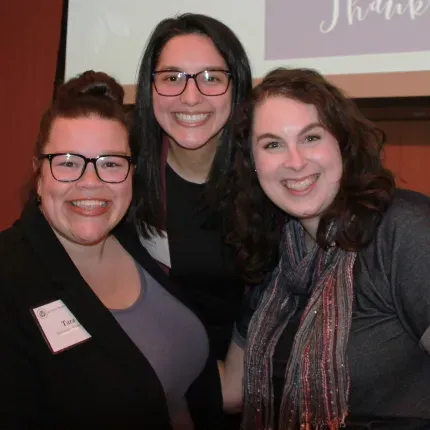 Three women smile for the camera at a fundraising event. 