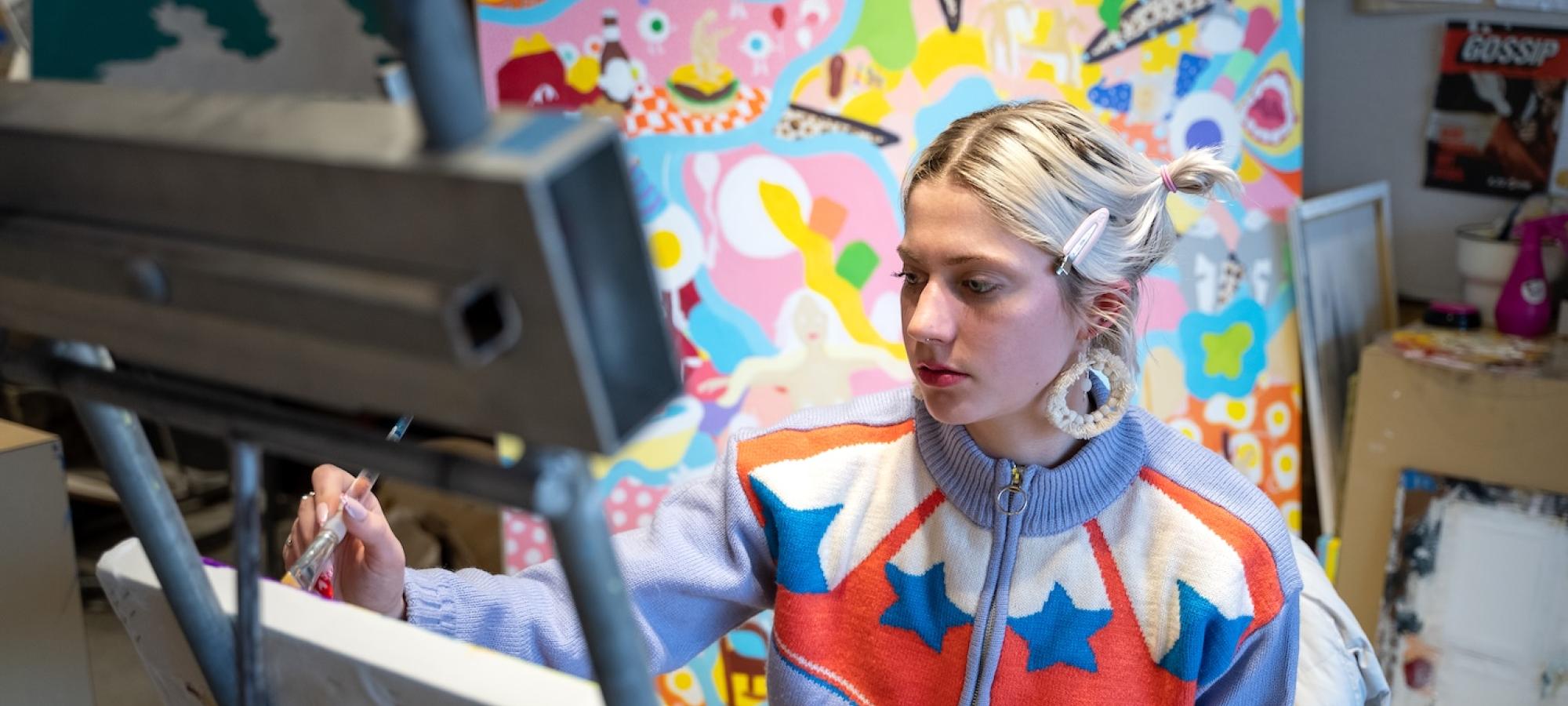 A young woman in colorful clothes paints a colorful painting.