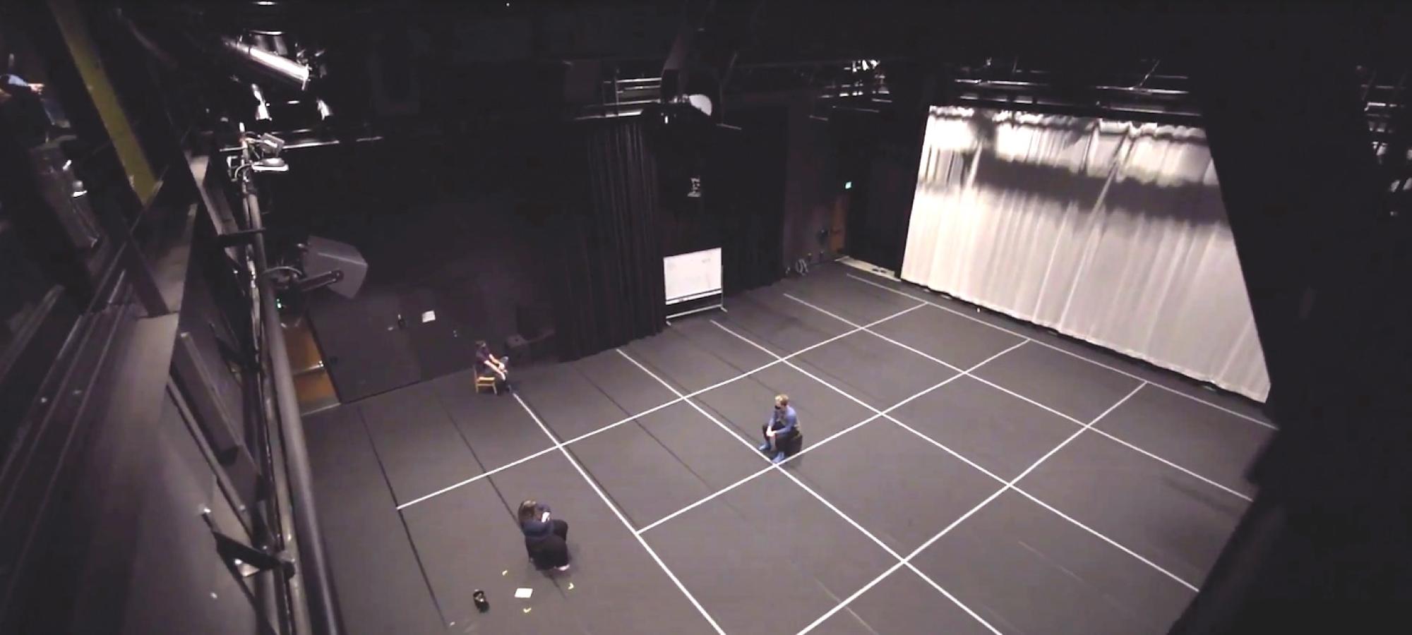 A long view of a black box theater with two performers. 
