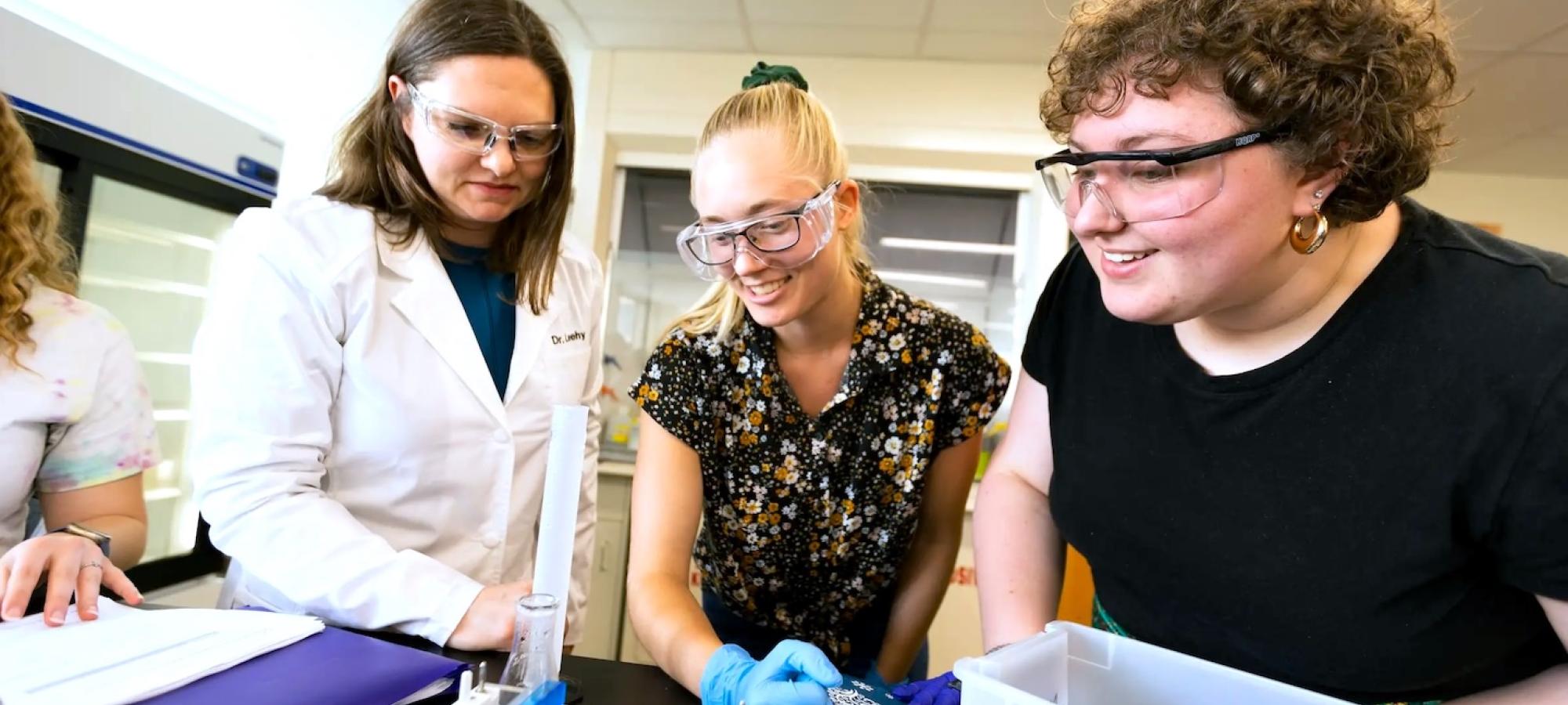 Two students engage in science with a professor. 