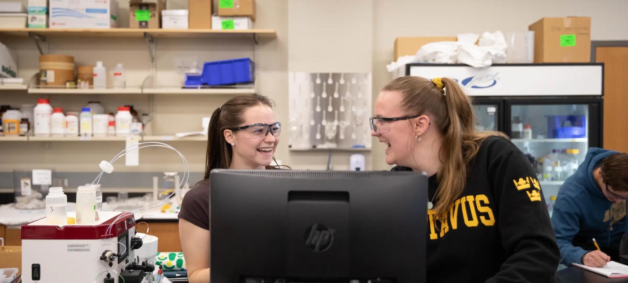 Two Gustavus Adolphus College biochemistry students laugh in a lab. 