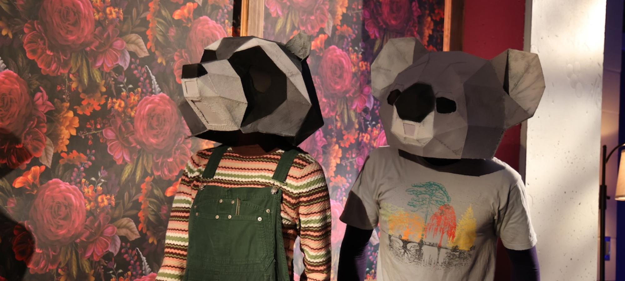 Two theatre students in animal heads look to the left. 