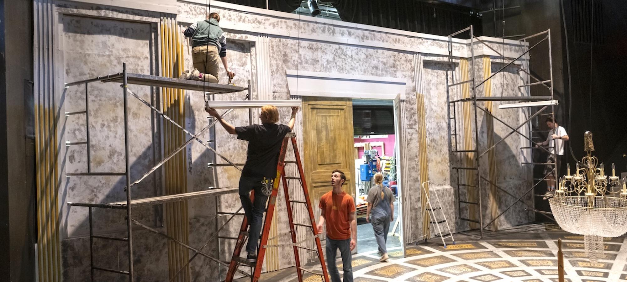 Theatre students on a ladder built a set. 
