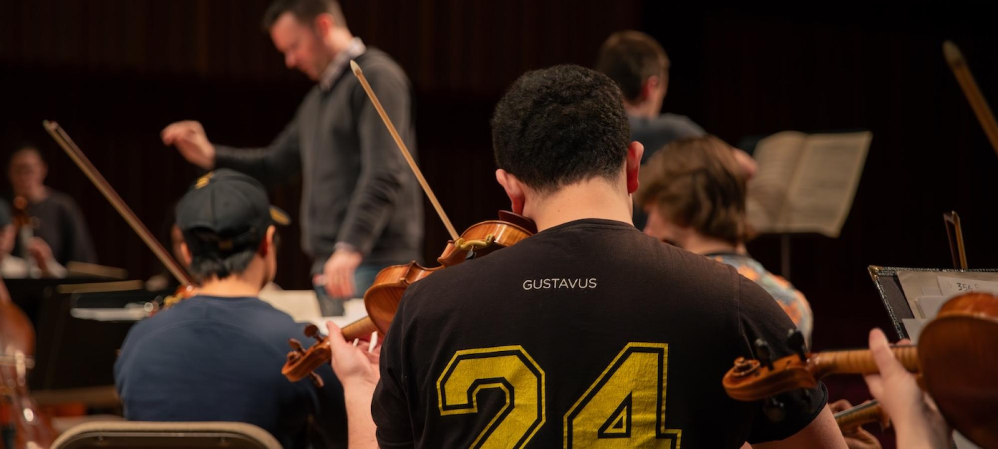 A student plays the violin as the conductor conducts. 