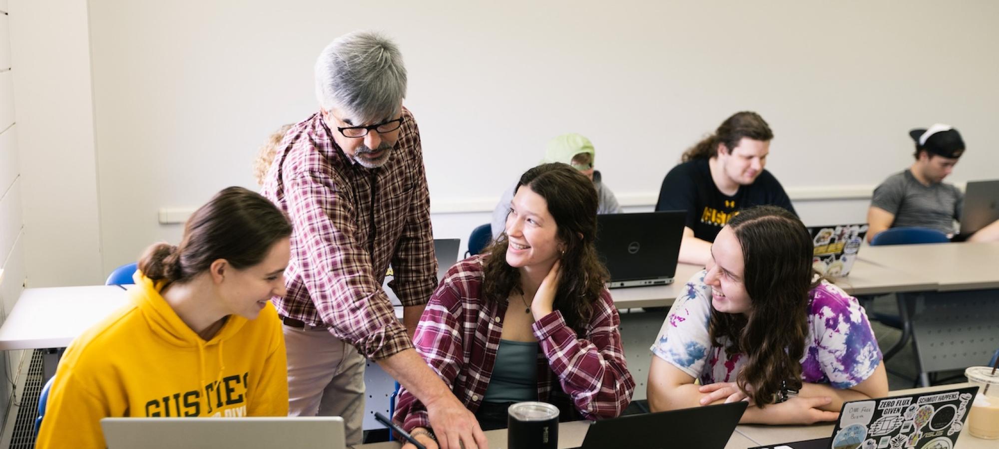 Students look at something a professor is pointing out in their work. 