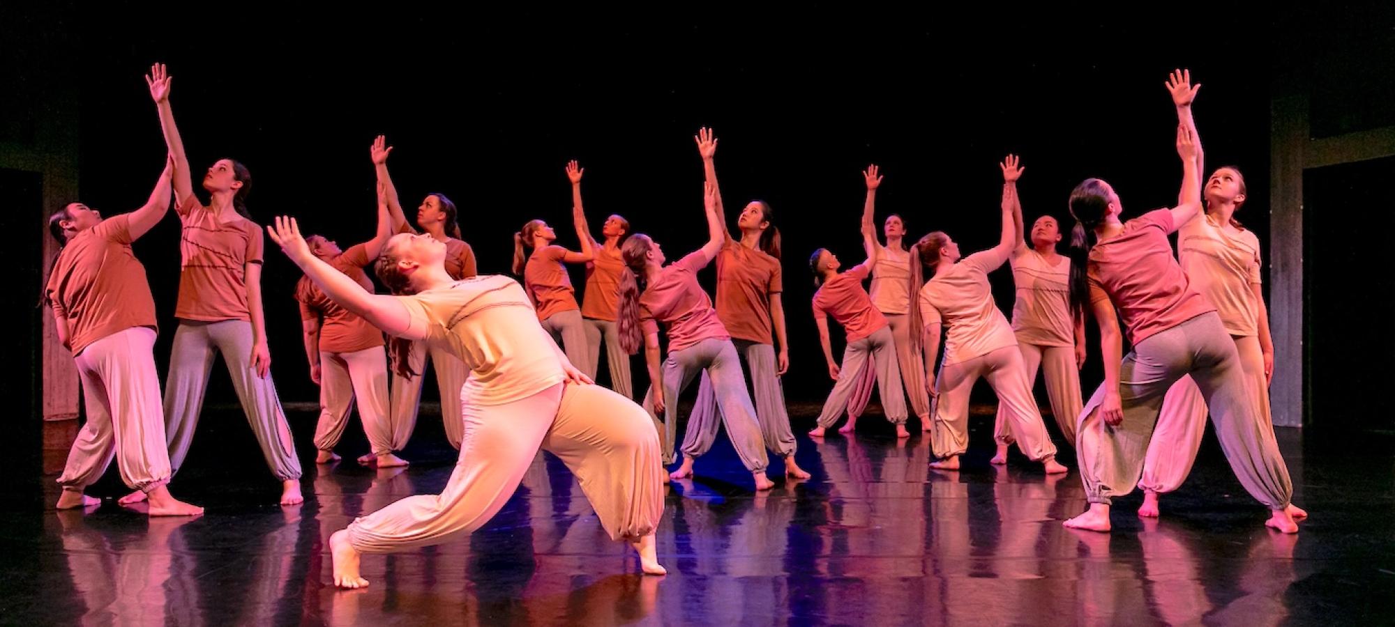 Multiple dancers on a stage reach toward the ceiling. 