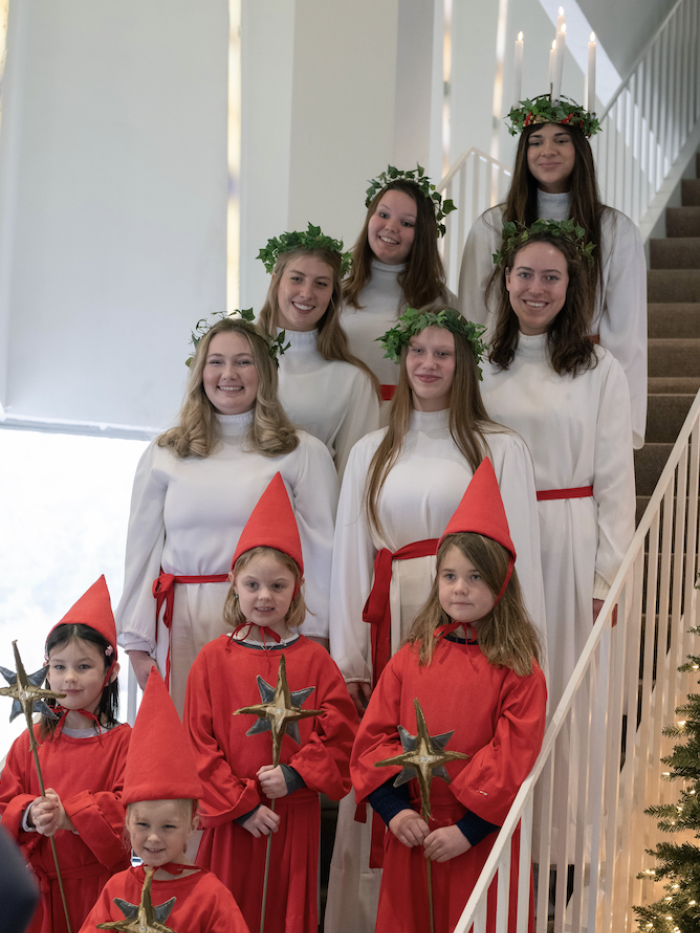St. Lucia Court made up of young women and children in white and red festive robes lined up on a staircase