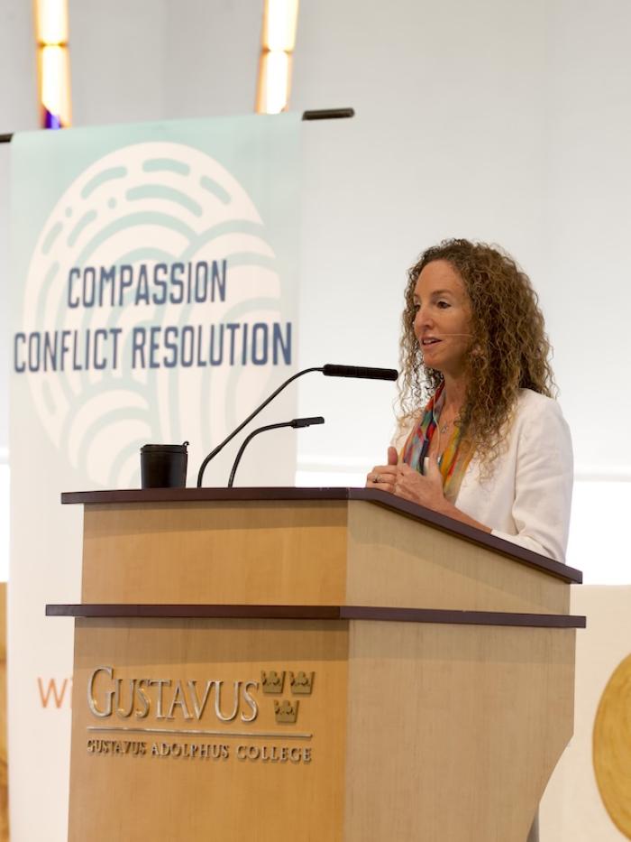 A woman speaks before a "Compassionate Conflict Resolution" sign
