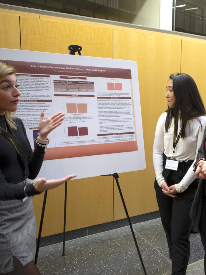 A student discusses her poster research with other students. 