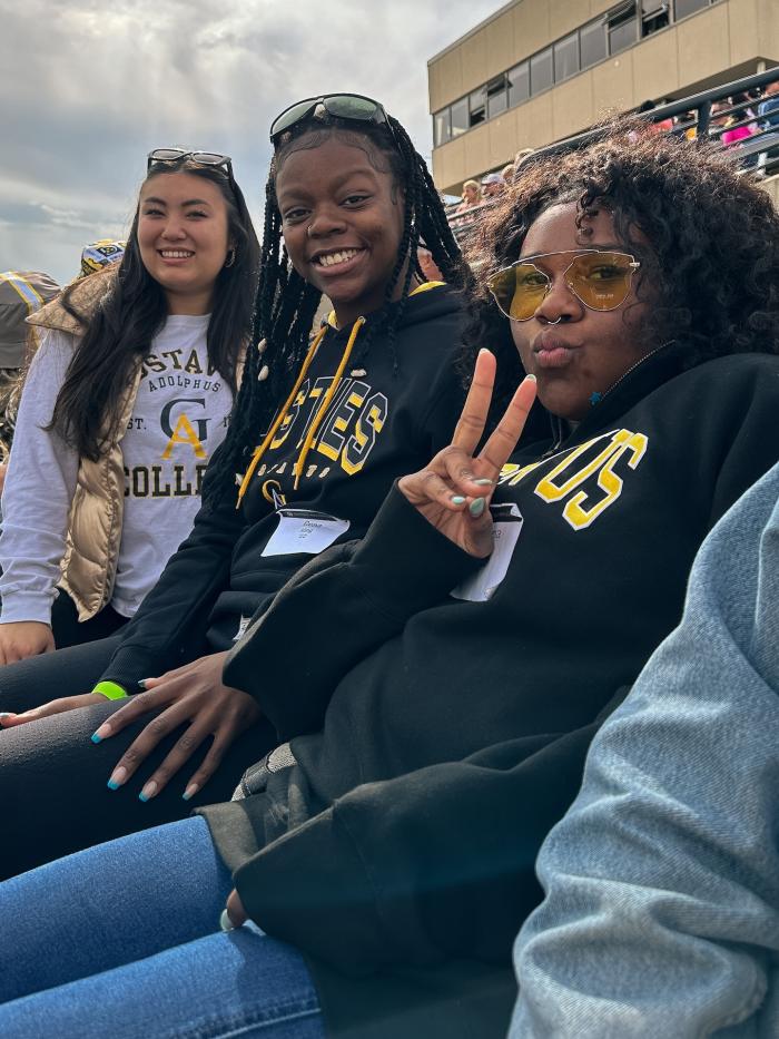 Three students mug for the camera at a college football game. 