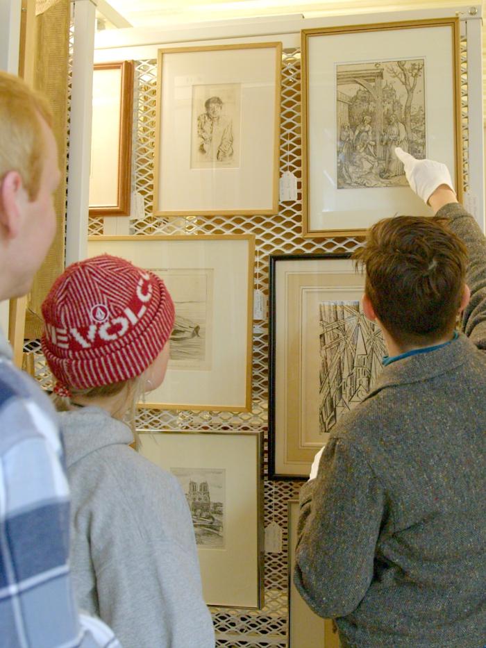 A professor points to a piece of framed art to show students something about it. 