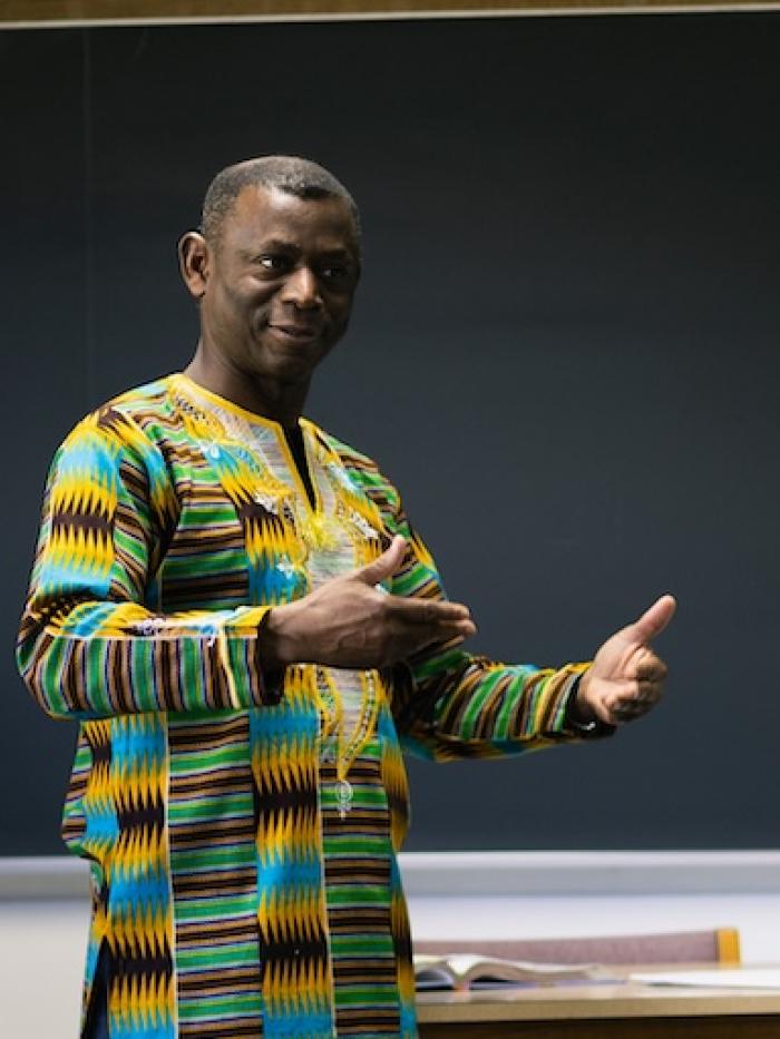 A French teacher in a colorful dashiki explains something to a class of college students. 