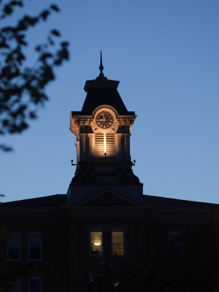 A college clocktower on an old main building at night. 