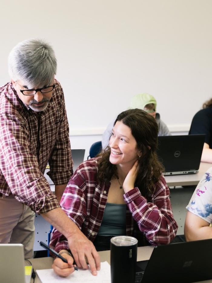 Students look at something a professor is pointing out in their work. 