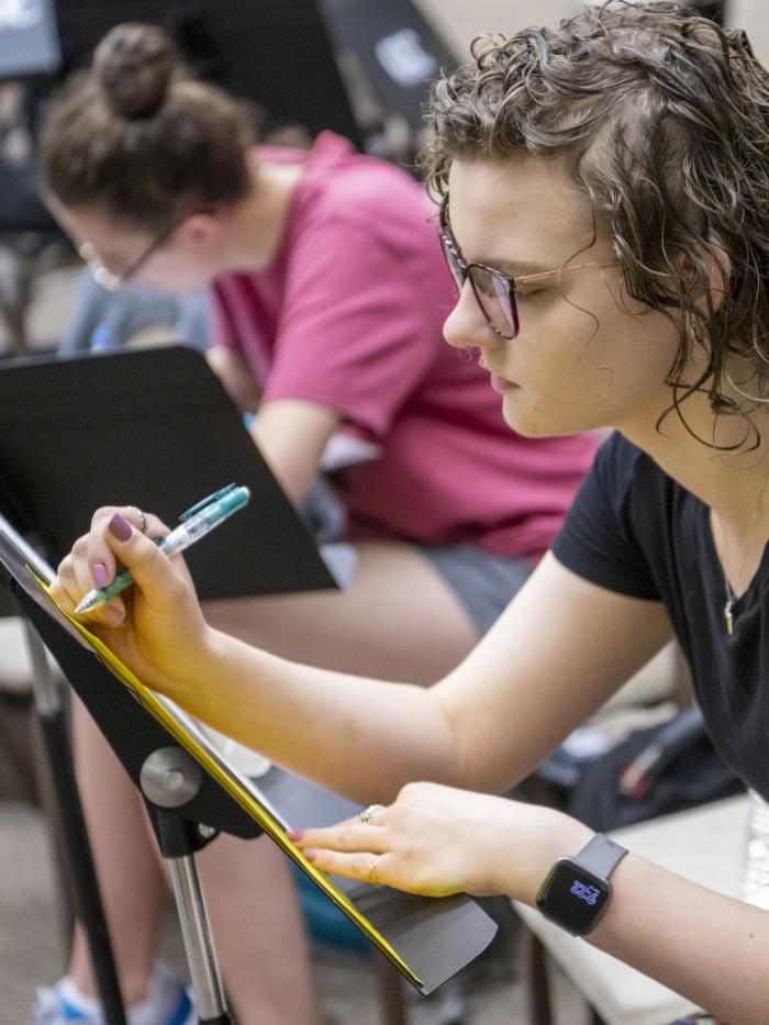 A student makes a note on her music placed on a music stand. 