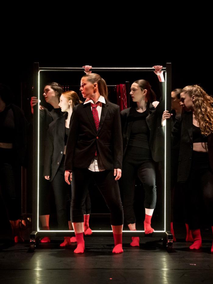 Several students in dark clothing and red socks dance within and outside a white box.