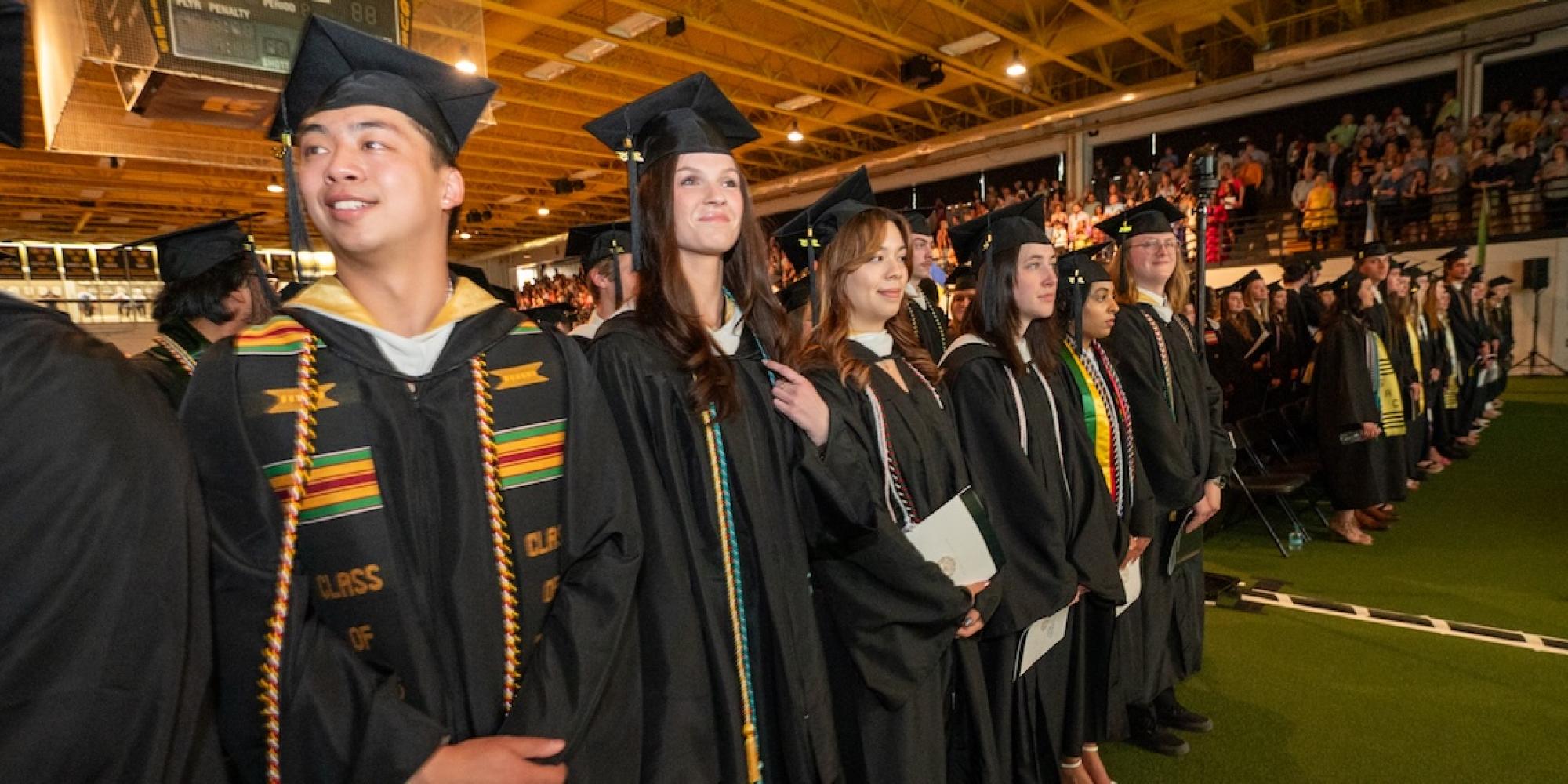 A row of college graduates stands to receive their diplomas. 